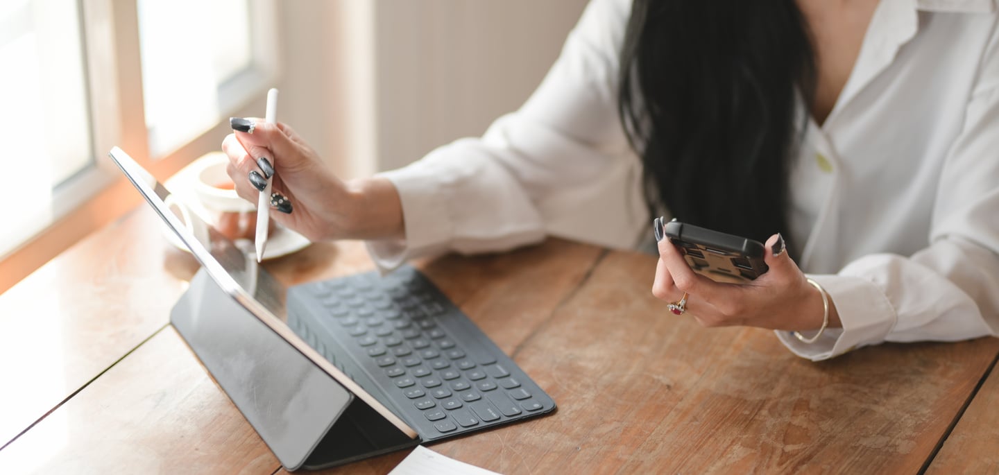 Person in White Long Sleeve Shirt Holding Black Smartphone While Using Tablet